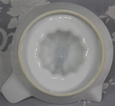 The base of a white ceramic saucer juicer with offset tab handle showing the footing