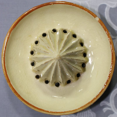 The reamer for a primitive image in brown on a beige ceramic juicer