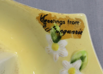 A partial souvenir sticker on a pastel yellow ceramic juicer with white flowers 