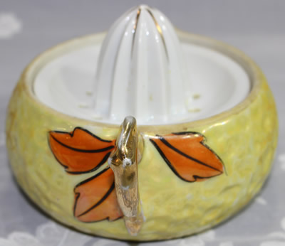 The handle area of a yellow with orange leaves and gold pear shape ceramic juicer