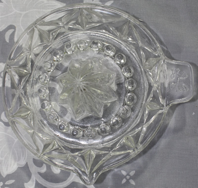 Top view of dragon on tab handle cross pattern clear glass saucer shape juicer