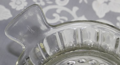 A close-up of the pattern on a fish tail shape handle clear glass saucer juicer