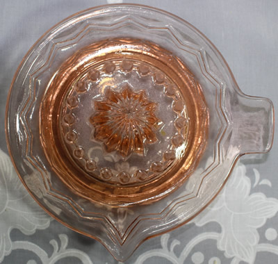 Top view of a pink glass zig-zag pattern saucer shape juicer