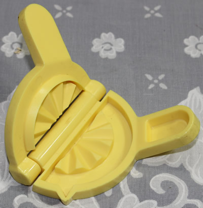An open small yellow plastic lemon wedge squeezer